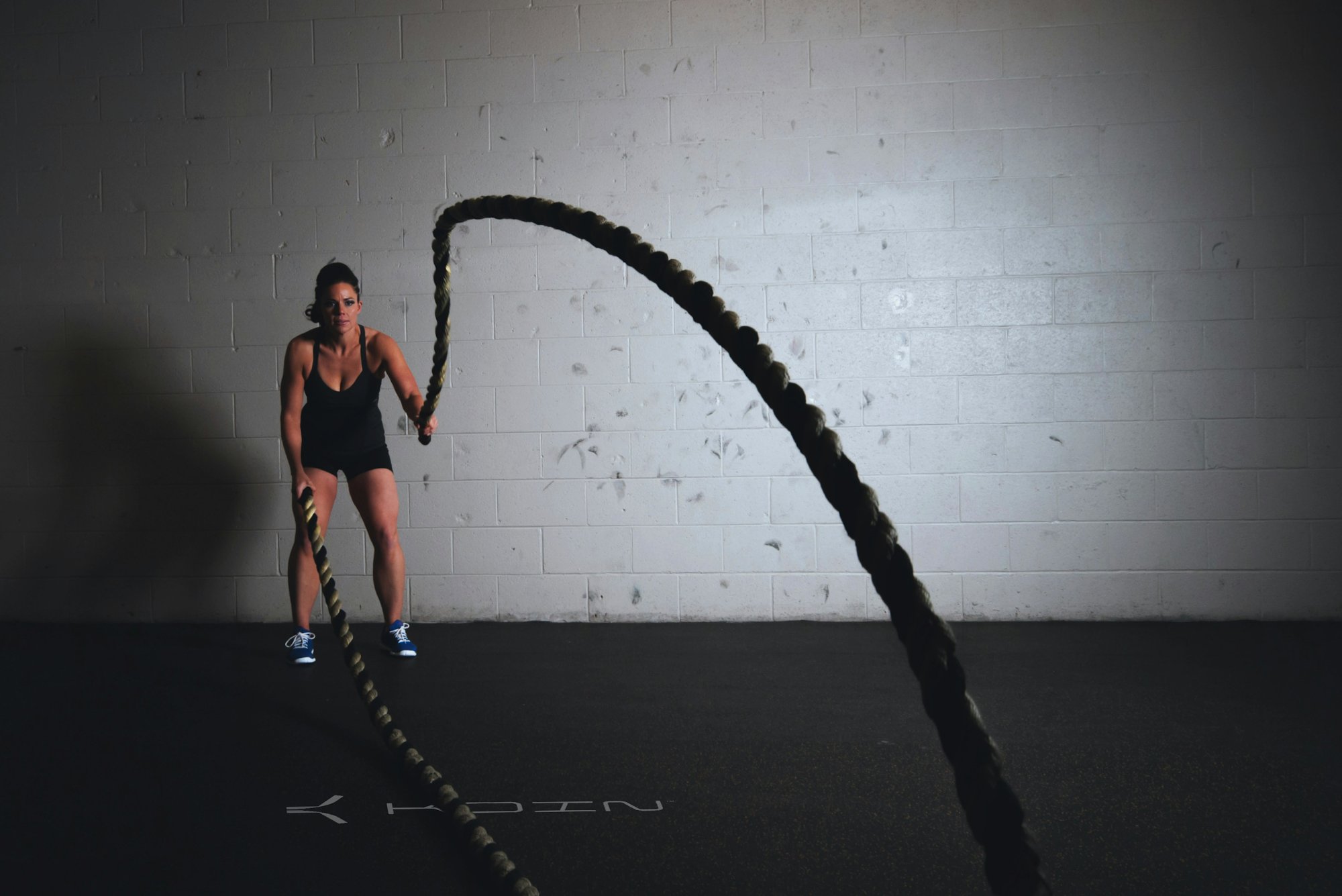 Athlete training with battle ropes, horizontal Koin logo on the floor